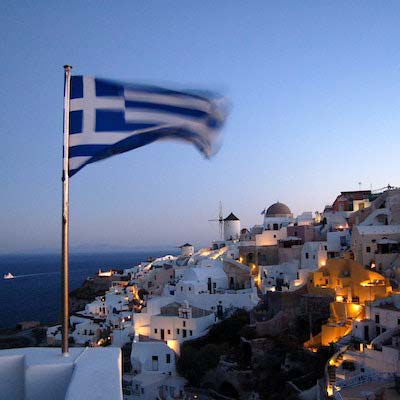 Greek flag flying over a coastal greek community at sunset"