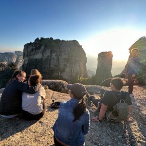 students watching sunset with backs to us in greece