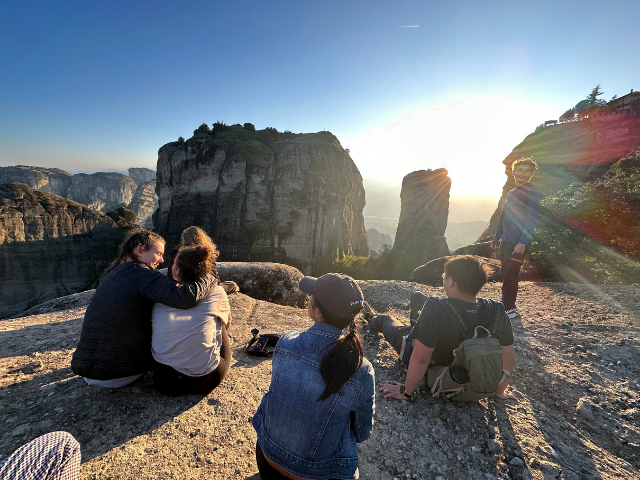 students watching sunset with backs to us in greece