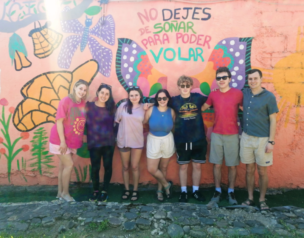 Smiling students pose for a group photo against a colorful wall in Antigua