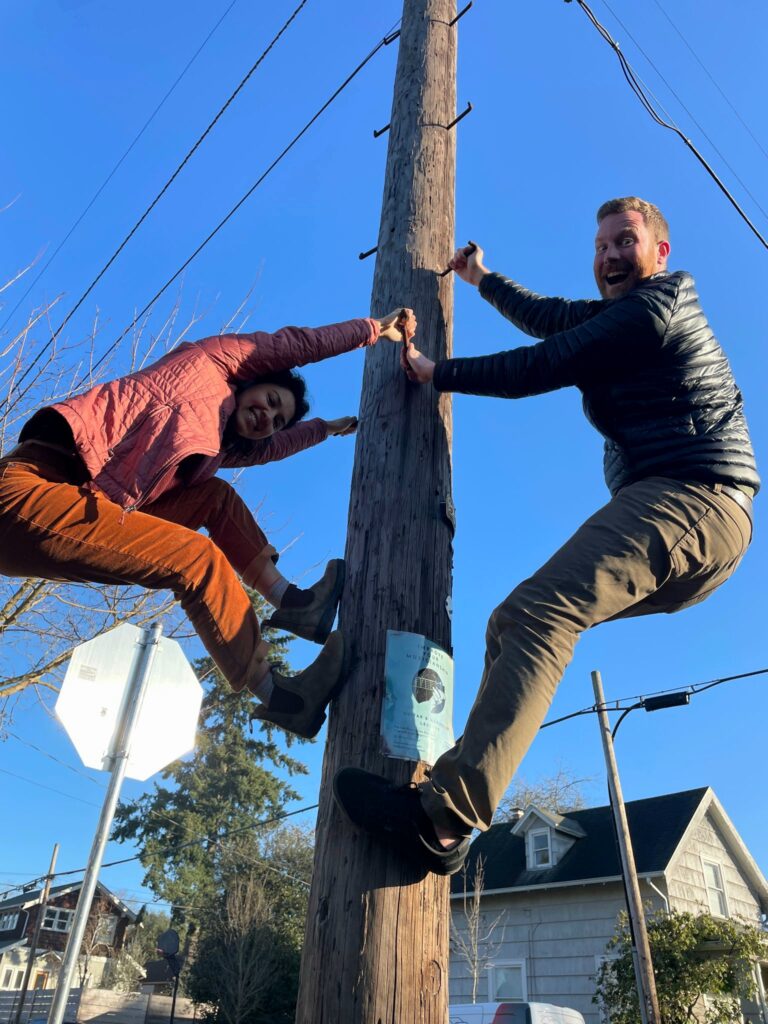 Two individuals ascending a wooden pole together