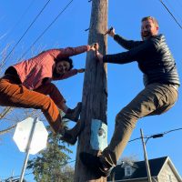 Two individuals ascending a wooden pole together